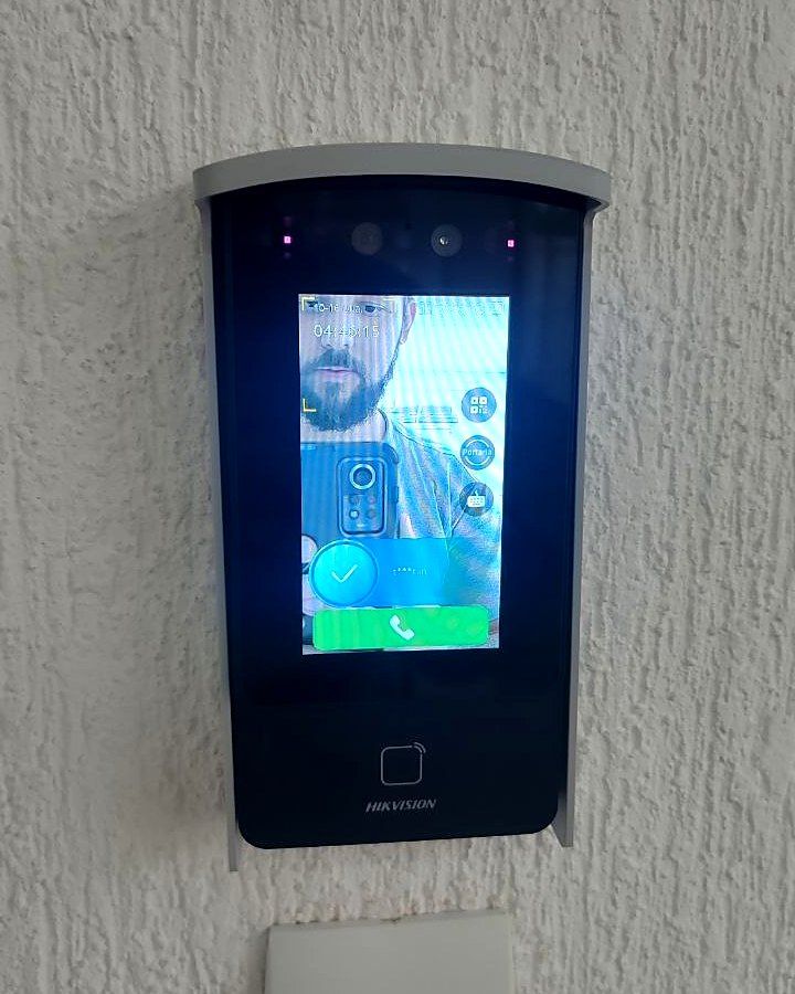 Leitor facial com aba de proteção instalado pela Tristan em parede texturizada, com o acesso liberado na tela