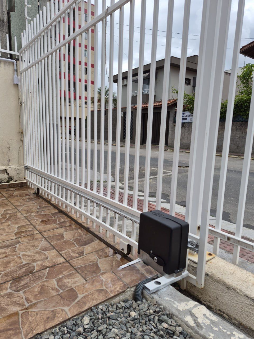 Motor de portão deslizante instalado pela Tristan junto a um portão de grade branco, sobre base de concreto
